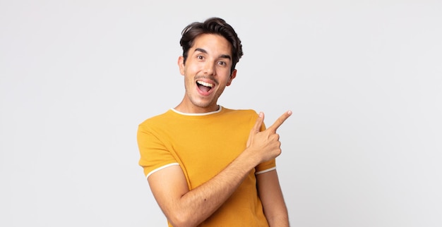 Hispanic handsome man looking excited and surprised pointing to the side and upwards to copy space