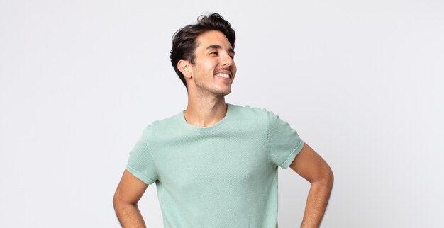 Hispanic handsome man looking happy, cheerful and confident, smiling proudly and looking to side with both hands on hips