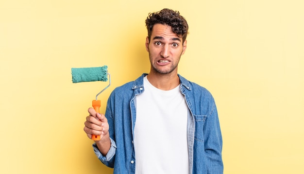 Hispanic handsome man looking puzzled and confused. roller paint concept