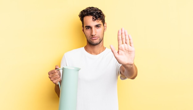 Hispanic handsome man looking serious showing open palm making stop gesture. coffee thermos concept