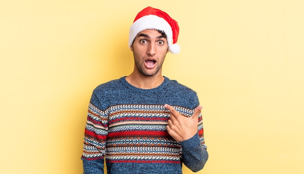 ヒスパニック系のハンサムな男は、口を大きく開いてショックを受けて驚いたように見え、自分を指しています。クリスマスのコンセプト