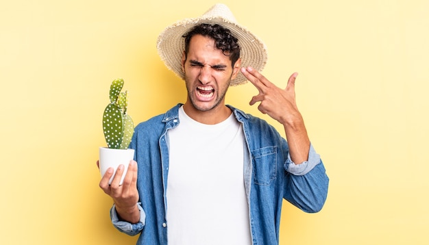 Hispanic handsome man looking unhappy and stressed, suicide gesture making gun sign farmer and cactus concept
