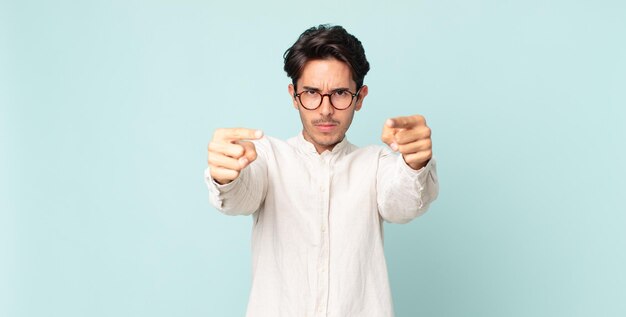 Hispanic handsome man pointing forward at camera with both fingers and angry expression, telling you to do your duty