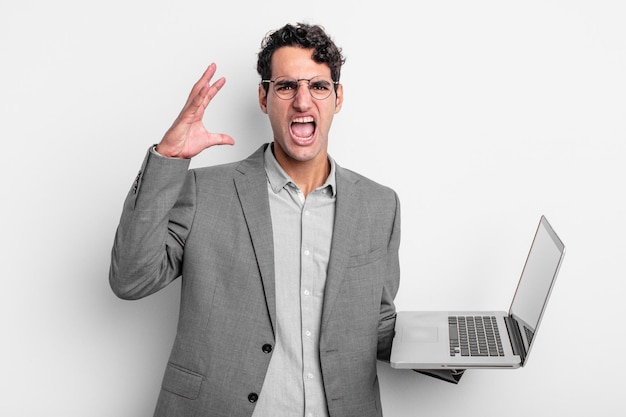 Hispanic handsome man screaming with hands up in the air. business and laptop concept