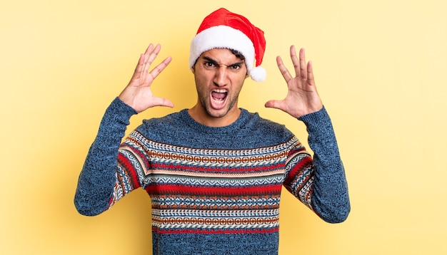 Hispanic handsome man screaming with hands up in the air. christmas concept