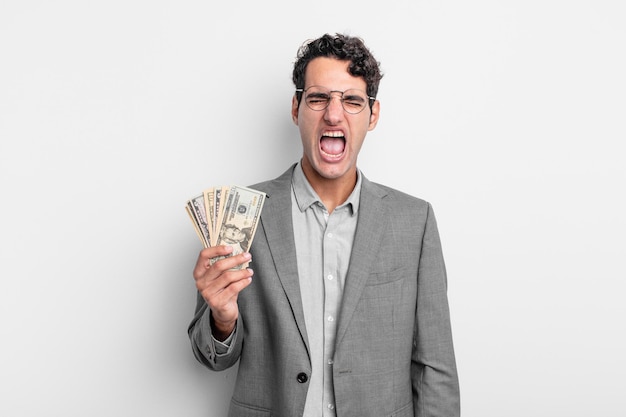 Hispanic handsome man shouting aggressively, looking very angry. business and dollar banknotes concept