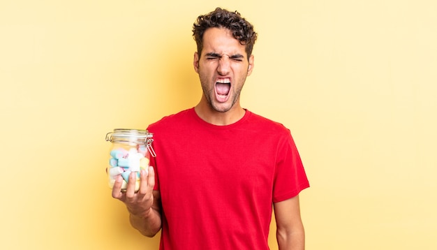 Hispanic handsome man shouting aggressively, looking very angry. candies concept