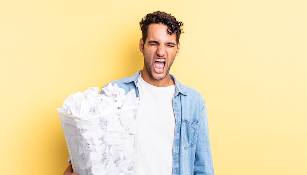 Hispanic handsome man shouting aggressively, looking very angry. paper balls trash concept