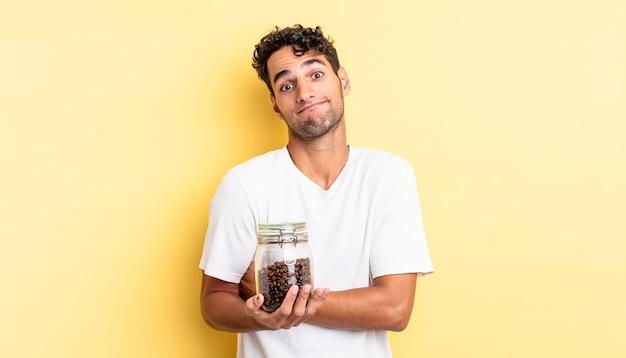 Hispanic handsome man shrugging, feeling confused and uncertain. coffee beans bottle