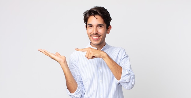 Hispanic handsome man smiling cheerfully and pointing to copy space on palm on the side, showing or advertising an object