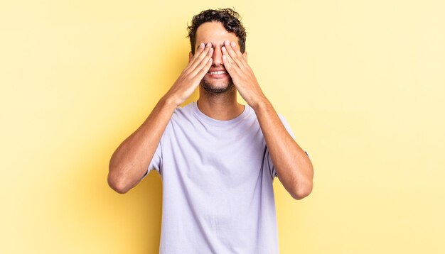 Hispanic handsome man smiling and feeling happy, covering eyes with both hands