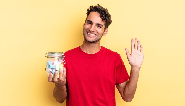 Hispanic handsome man smiling happily, waving hand, welcoming and greeting you. candies concept