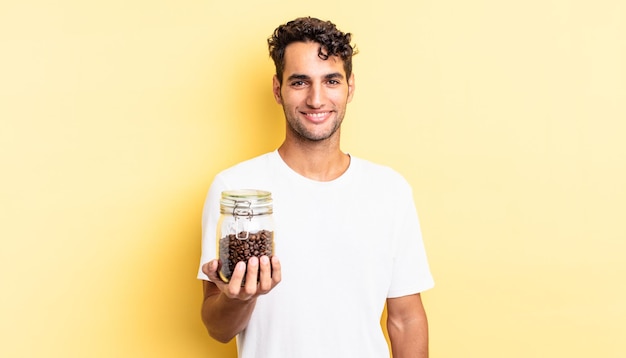 Hispanic handsome man smiling happily with a hand on hip and confident. coffee beans bottle