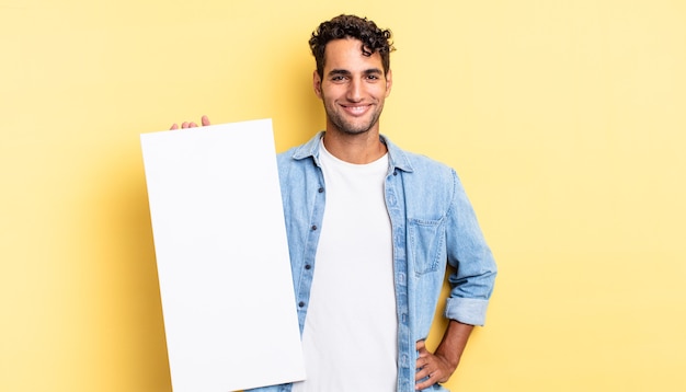 Hispanic handsome man smiling happily with a hand on hip and confident. empty canvas concept