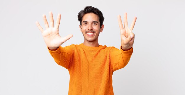 Hispanic handsome man smiling and looking friendly, showing number eight or eighth with hand forward, counting down