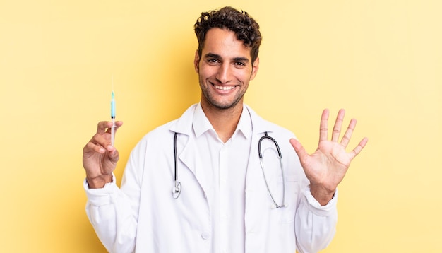 Hispanic handsome man smiling and looking friendly, showing number five physician and srynge concept