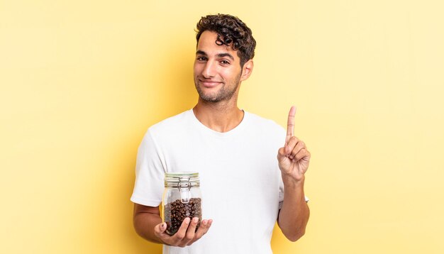 Hispanic handsome man smiling and looking friendly, showing number one. coffee beans bottle