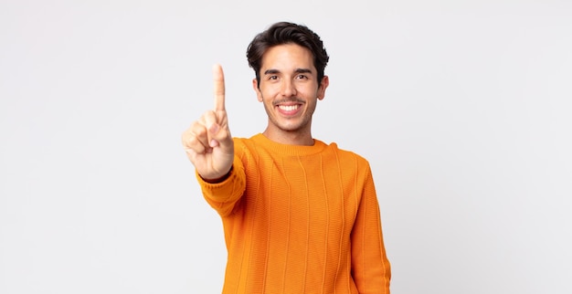 Hispanic handsome man smiling and looking friendly, showing number one or first with hand forward, counting down