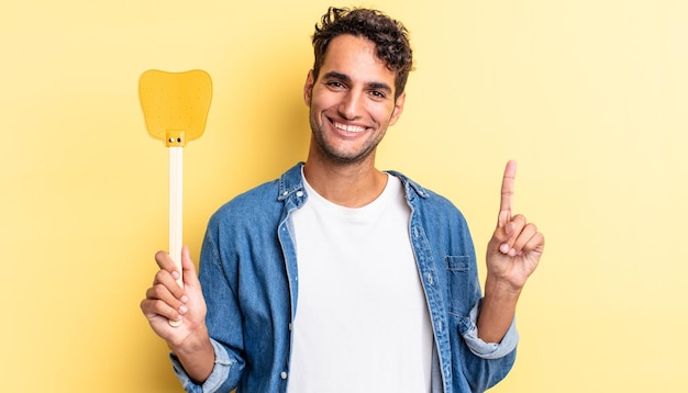 Hispanic handsome man smiling and looking friendly, showing number one. kills flies concept