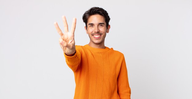 hispanic handsome man smiling and looking friendly, showing number three or third with hand forward, counting down