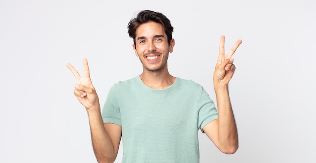 Hispanic handsome man smiling and looking happy, friendly and satisfied, gesturing victory or peace with both hands