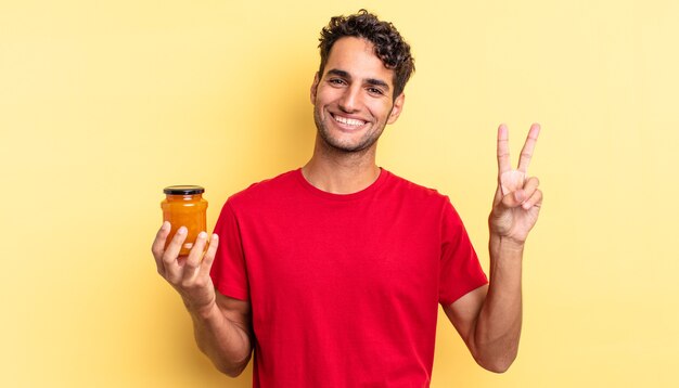 Hispanic handsome man smiling and looking happy, gesturing victory or peace. peach jam