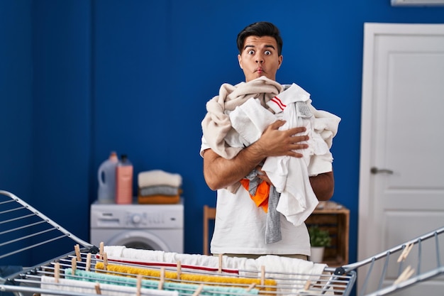 Hispanic man hanging clothes at clothesline making fish face with mouth and squinting eyes crazy and comical