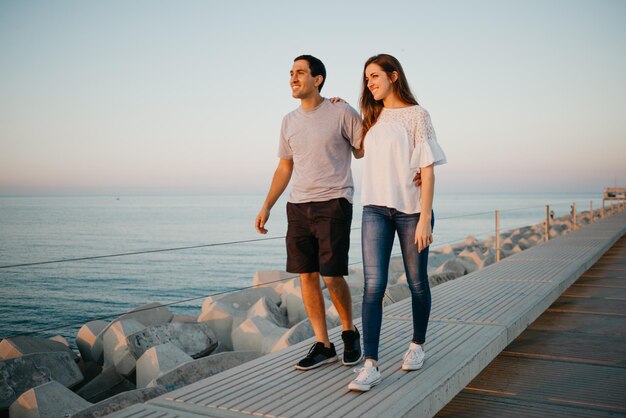 ヒスパニック系の男性と彼のガールフレンドがスペインの防波堤を散歩しています