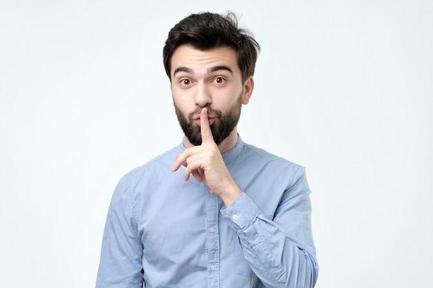 Hispanic man placing finger on lips as if to say shhhhh be quiet silence