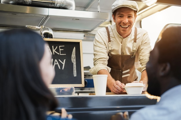 Photo hispanic man serving take away food inside food truck - focus on chef face