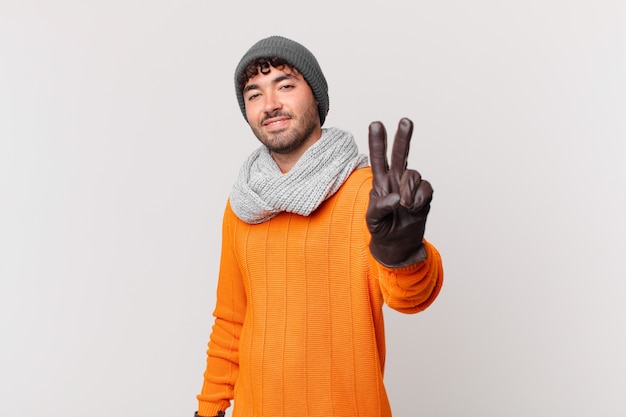 Hispanic man smiling and looking happy, carefree and positive, gesturing victory or peace with one hand