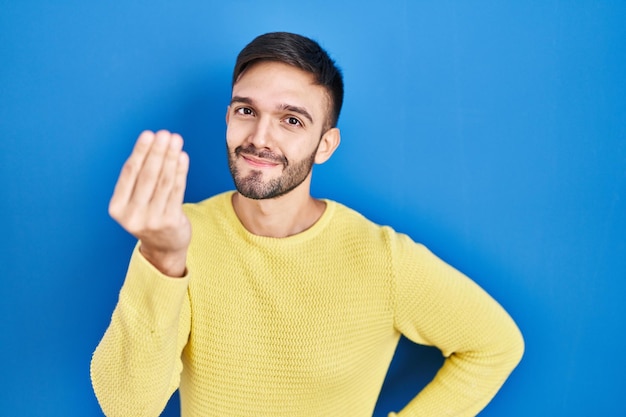 Hispanic man standing over blue background doing italian gesture with hand and fingers confident expression