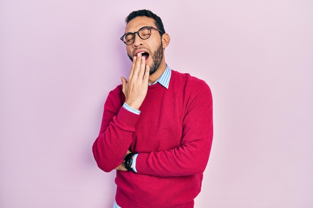 Hispanic man with beard wearing business shirt and glasses bored yawning tired covering mouth with hand restless and sleepiness