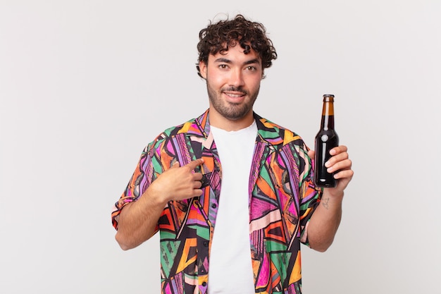 Hispanic man with beer feeling happy, surprised and proud, pointing to self with an excited, amazed look