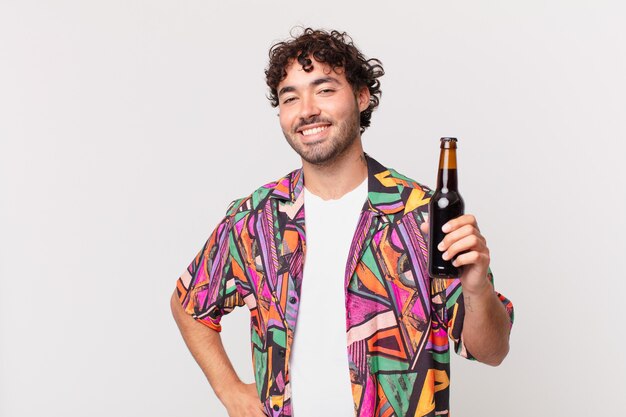 Hispanic man with beer smiling happily with a hand on hip and confident, positive, proud and friendly attitude