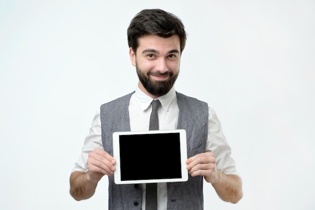 Hispanic man with black beard shows tablet computer with blank screen