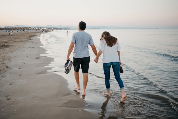 A Hispanic man with his girlfriend are strolling on a sandy beach in Valencia