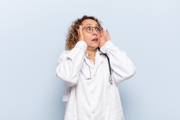 Hispanic middle age woman feeling happy, excited and surprised, looking to the side with both hands on face