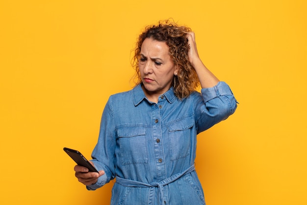 Photo hispanic middle age woman feeling puzzled and confused, scratching head and looking to the side