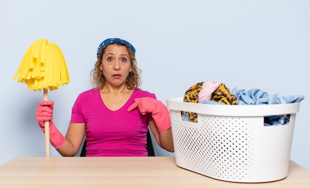 hispanic middle age woman looking shocked and surprised with mouth wide open, pointing to self