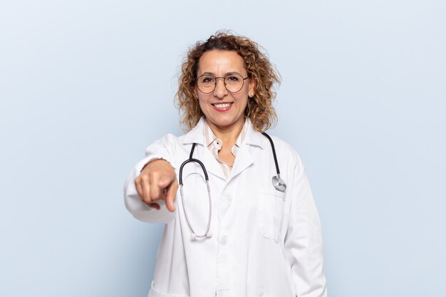 Hispanic middle age woman pointing at camera with a satisfied, confident, friendly smile, choosing you