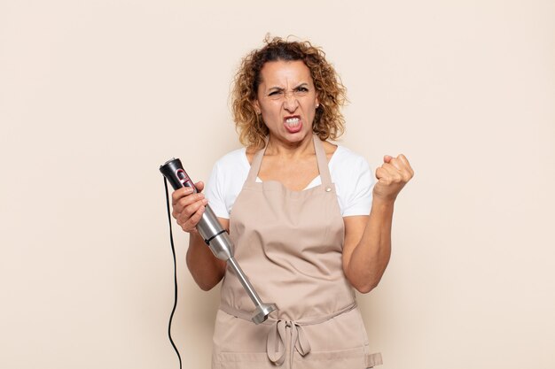 Hispanic middle age woman shouting aggressively with an angry expression or with fists clenched celebrating success