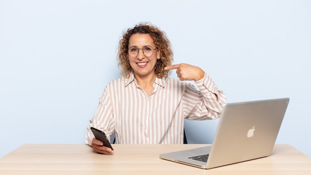 Hispanic middle age woman smiling confidently pointing to own broad smile, positive, relaxed, satisfied attitude