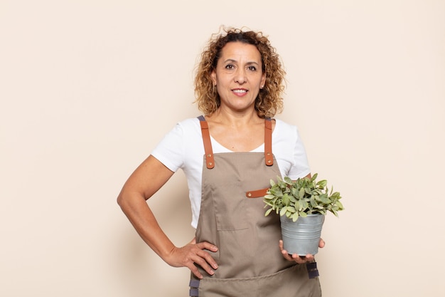 hispanic middle age woman smiling happily with a hand on hip and confident, positive, proud and friendly attitude