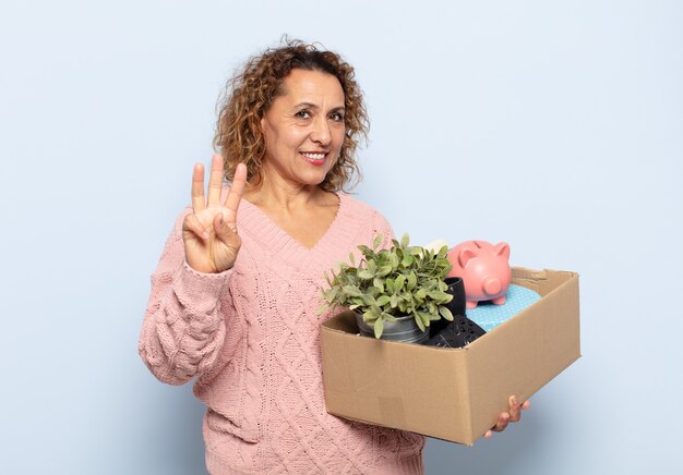 Hispanic middle age woman smiling and looking friendly, showing number three or third with hand forward, counting down