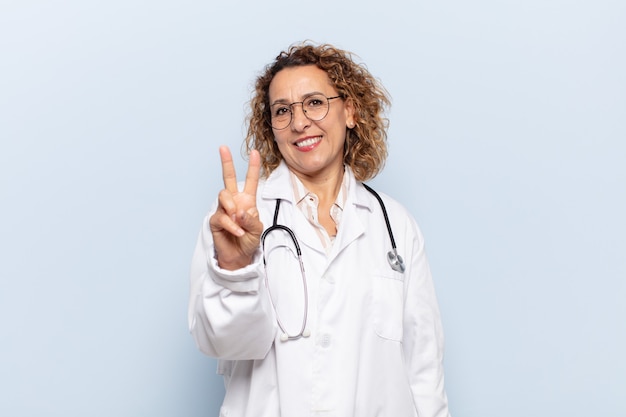 Hispanic middle age woman smiling and looking happy, carefree and positive, gesturing victory or peace with one hand