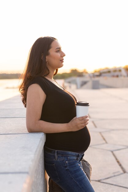 Испаноязычная беременная женщина пьет кофе на вынос на открытом воздухе