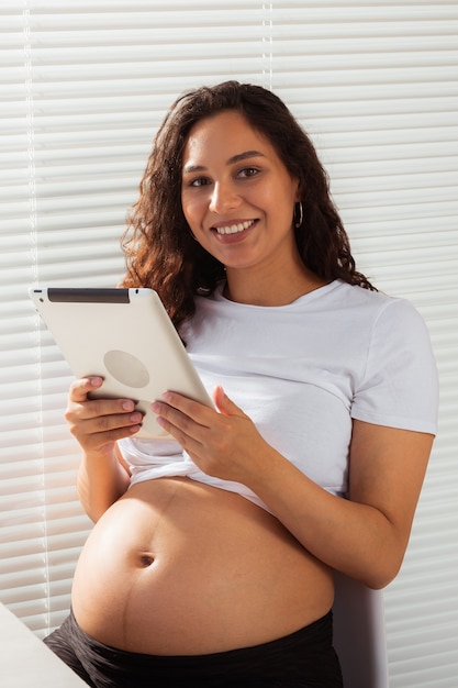 아침 식사 동안 디지털 태블릿을 사용하는 히스패닉계 임산부. 기술, 임신 및 출산 휴가.