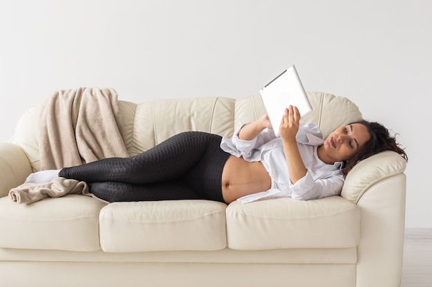 Hispanic pregnant woman using tablet computer while lying on sofa at home pregnancy and information