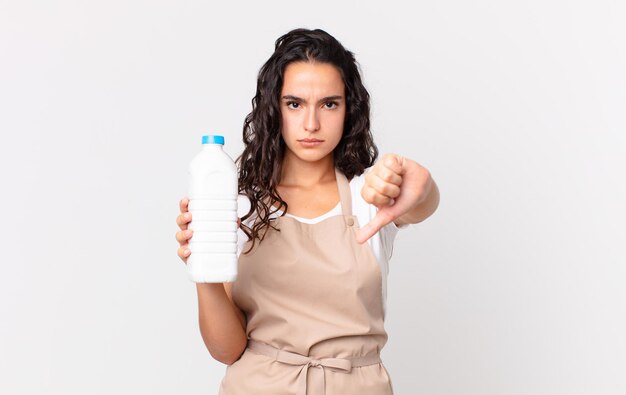 Hispanic pretty chef woman feeling cross,showing thumbs down and holding a milk bottle